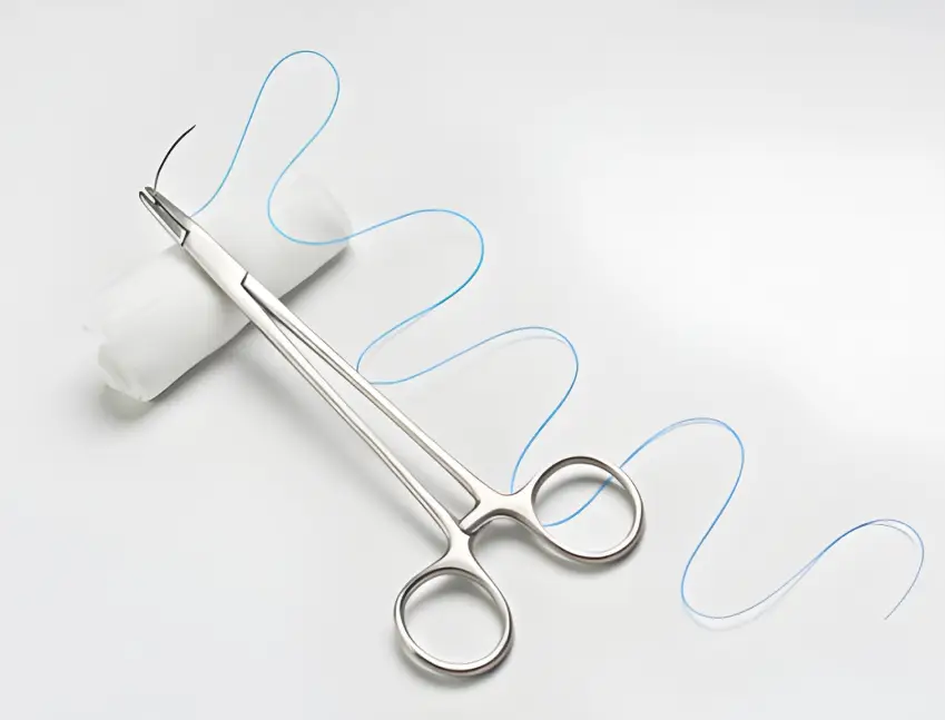 A polished surgical needle holder with a needle and thread, representing instruments that benefit from ARKA's coatings for smooth operation and long-lasting performance.