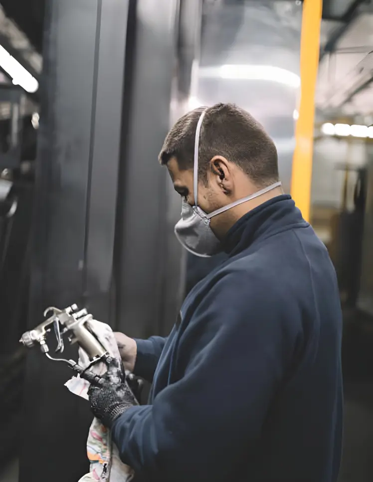 Industrial worker wearing a protective mask and gloves while cleaning a spray gun in a factory.