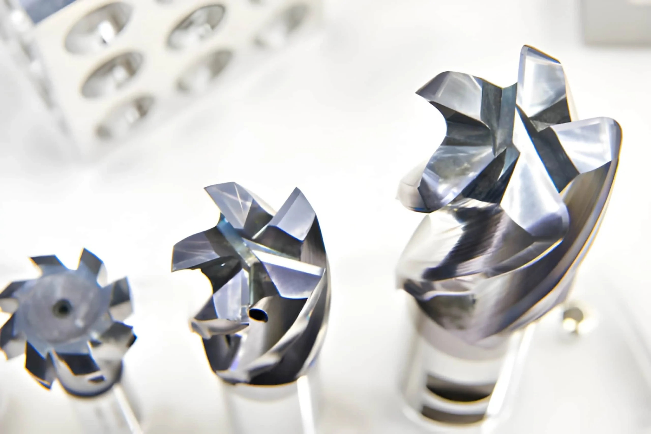 Three different sizes of high-performance solid carbide end mills for CNC machining, showing the sharp cutting flutes and polished steel finish from a top-down perspective.